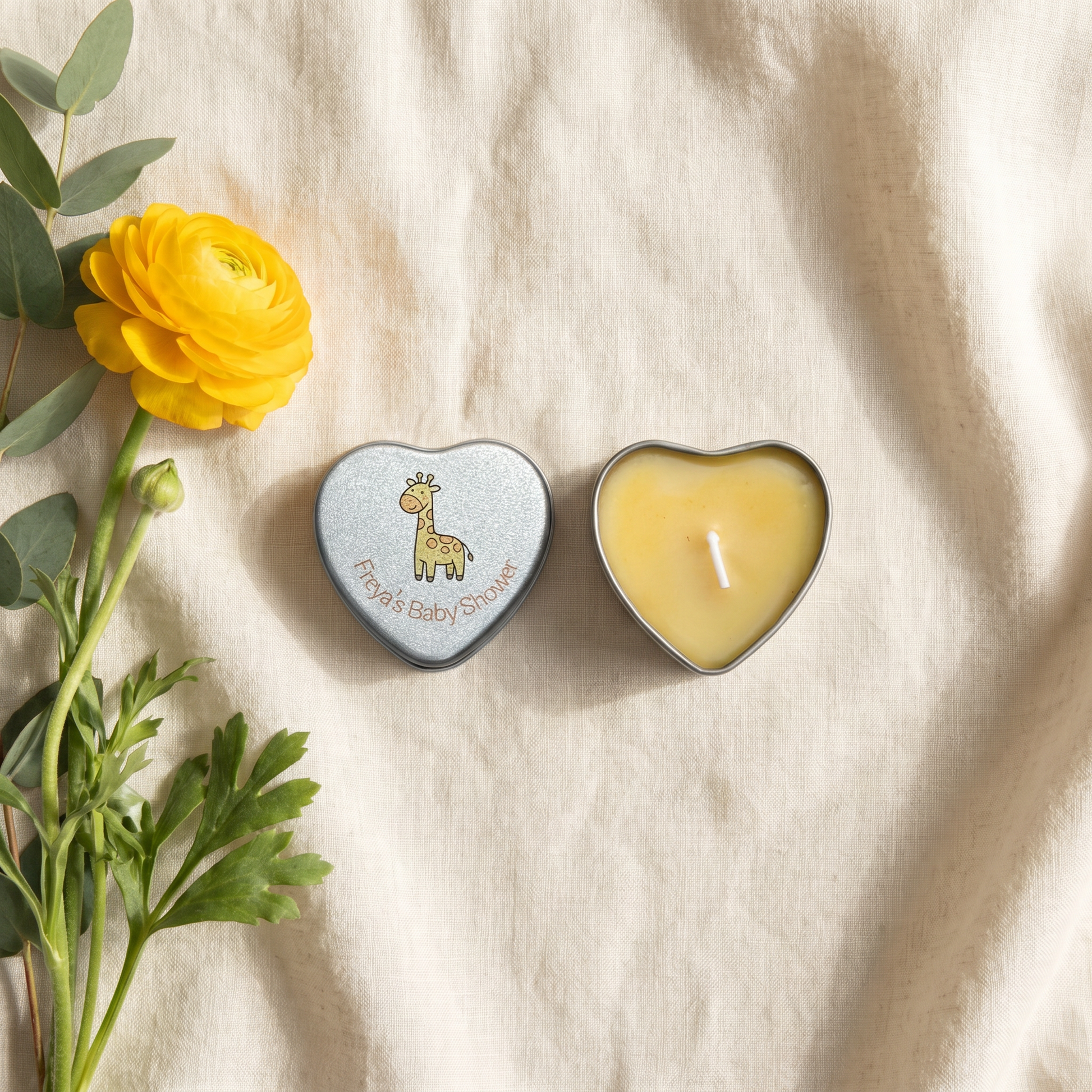 Personalised yellow baby shower candle favour — silver heart tin open showing yellow wax candle with giraffe lid design, styled with yellow ranunculus flowers