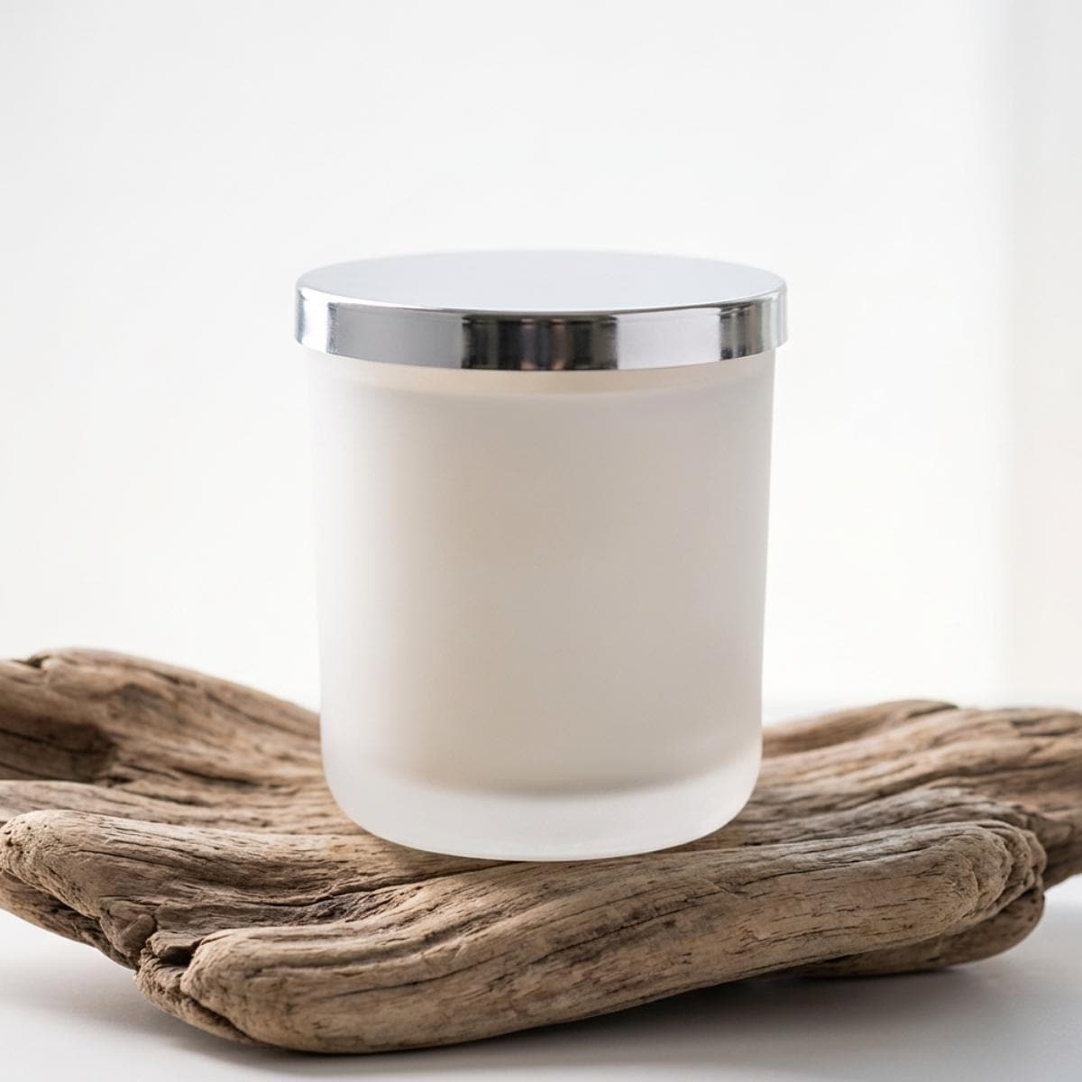 Hand-poured white frosted glass candle with polished silver-coloured lid on natural driftwood, before personalisation.