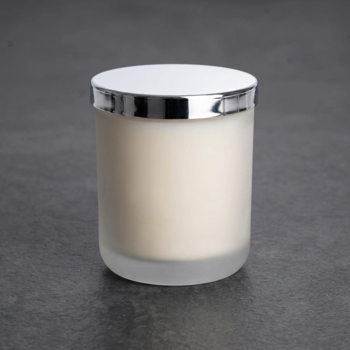 White frosted glass candle jar with silver-coloured lid photographed on a plain grey background.