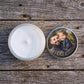 personalised candle shown open on rustic wooden boards, with natural wax and cotton wick visible and the printed photo lid resting alongside.