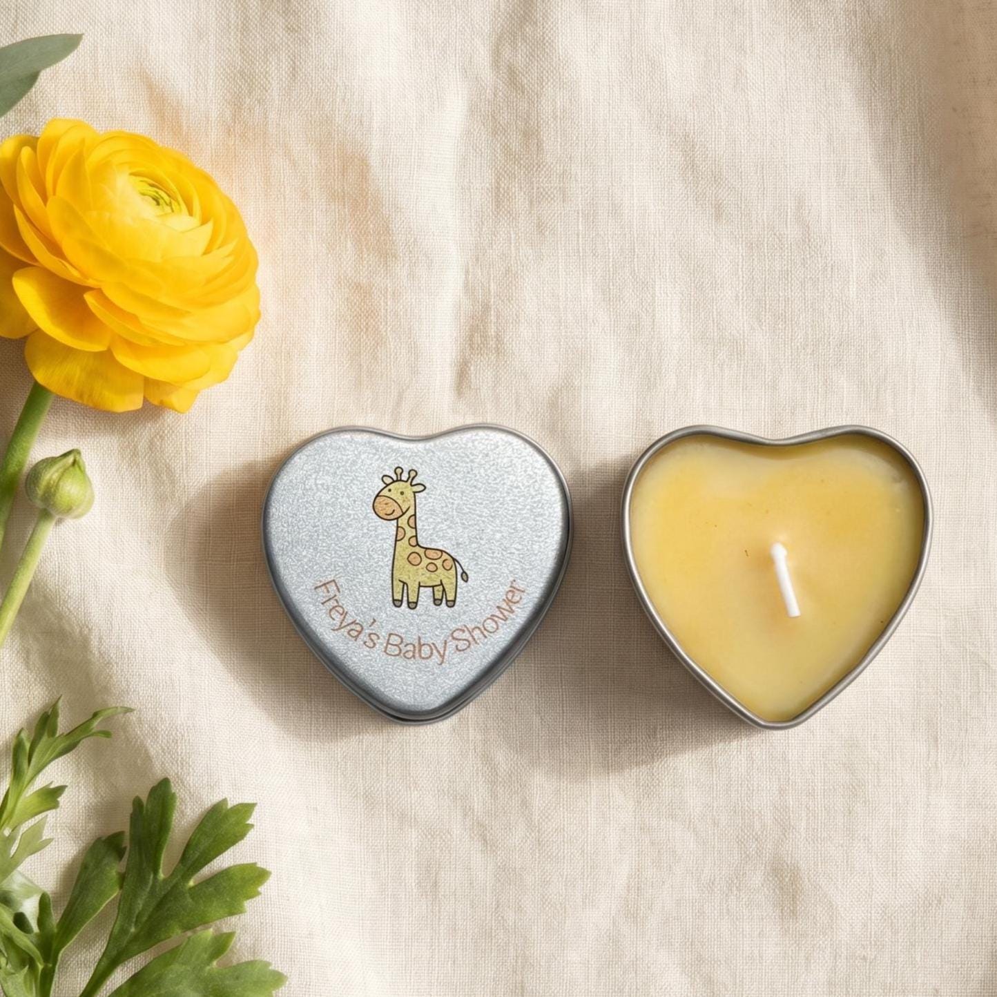 Personalised yellow baby shower candle favour — silver heart tin open showing yellow wax candle with giraffe lid design, styled with yellow ranunculus flowers