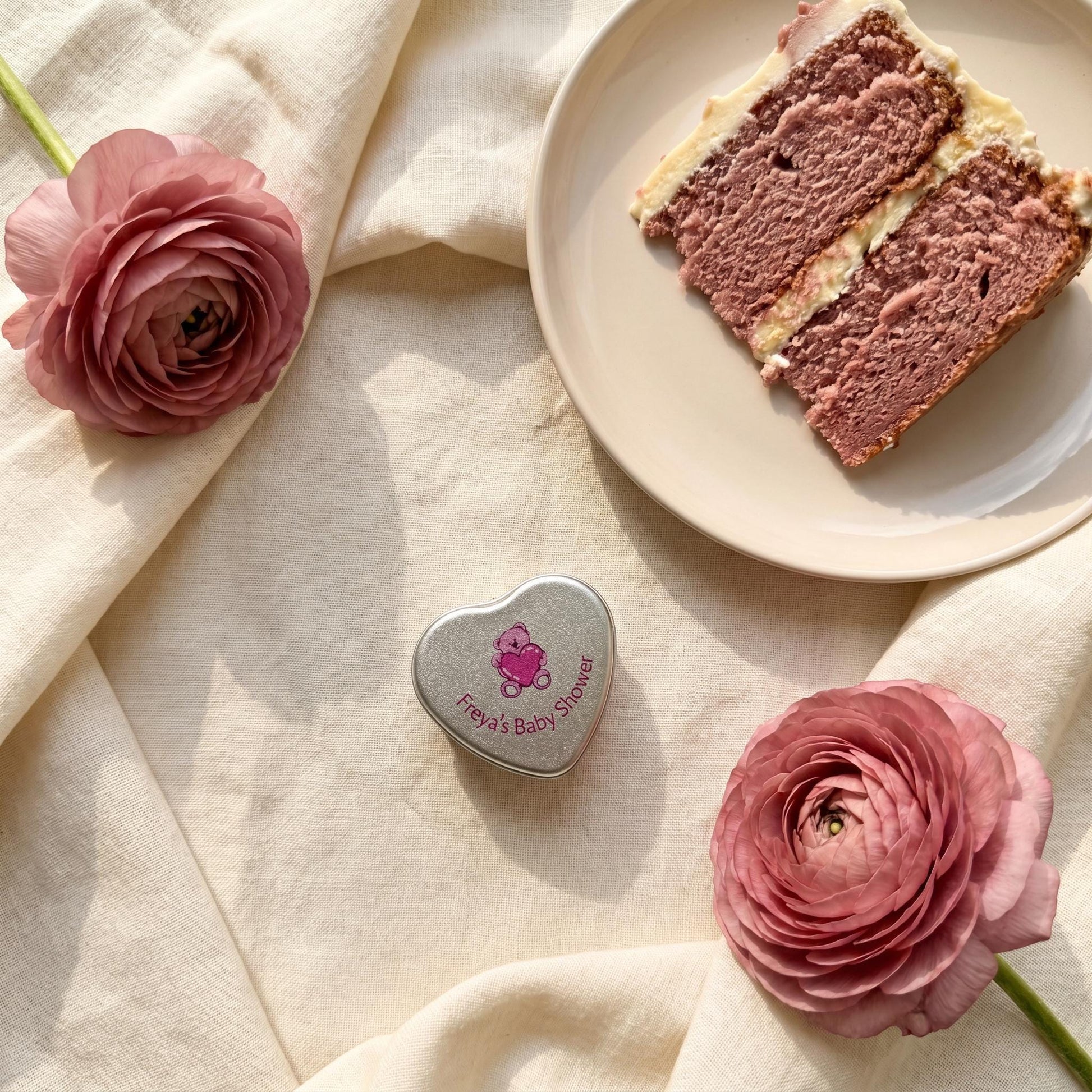 Personalised pink baby shower heart tin candle favour styled with pink cake and ranunculus flowers — teddy bear lid design