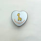 Close-up of personalised baby shower heart tin candle lid with giraffe design — yellow theme