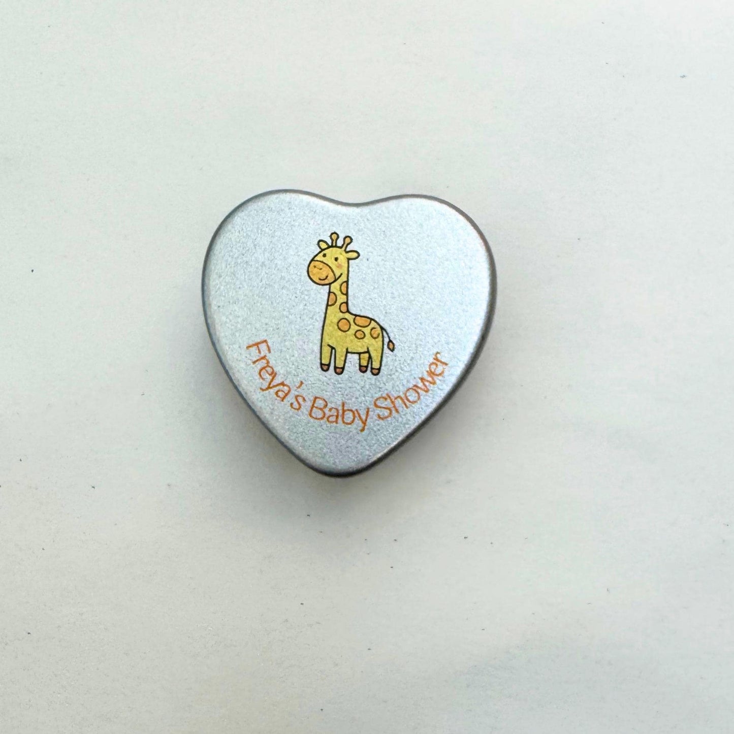 Close-up of personalised baby shower heart tin candle lid with giraffe design — yellow theme